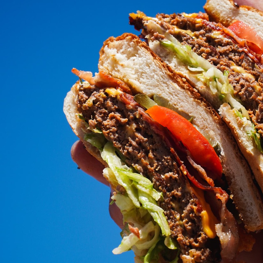 Signature smash burger with bacon, cheese, lettuce and tomato held against a blue sky